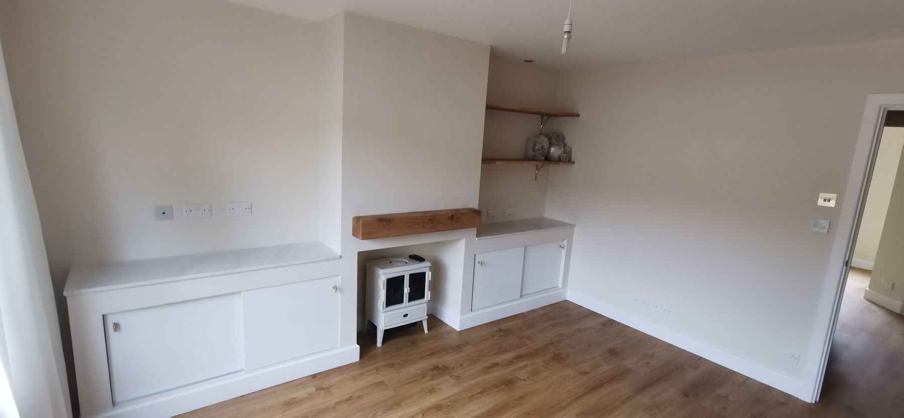 Wide view of a country-style living room with fitted cabinets either side of a log burner