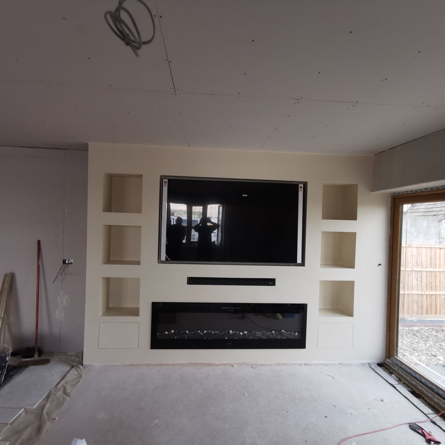 Media wall plastered and skimmed, ready for paint, with fireplace and TV recess either side of bifold doors
