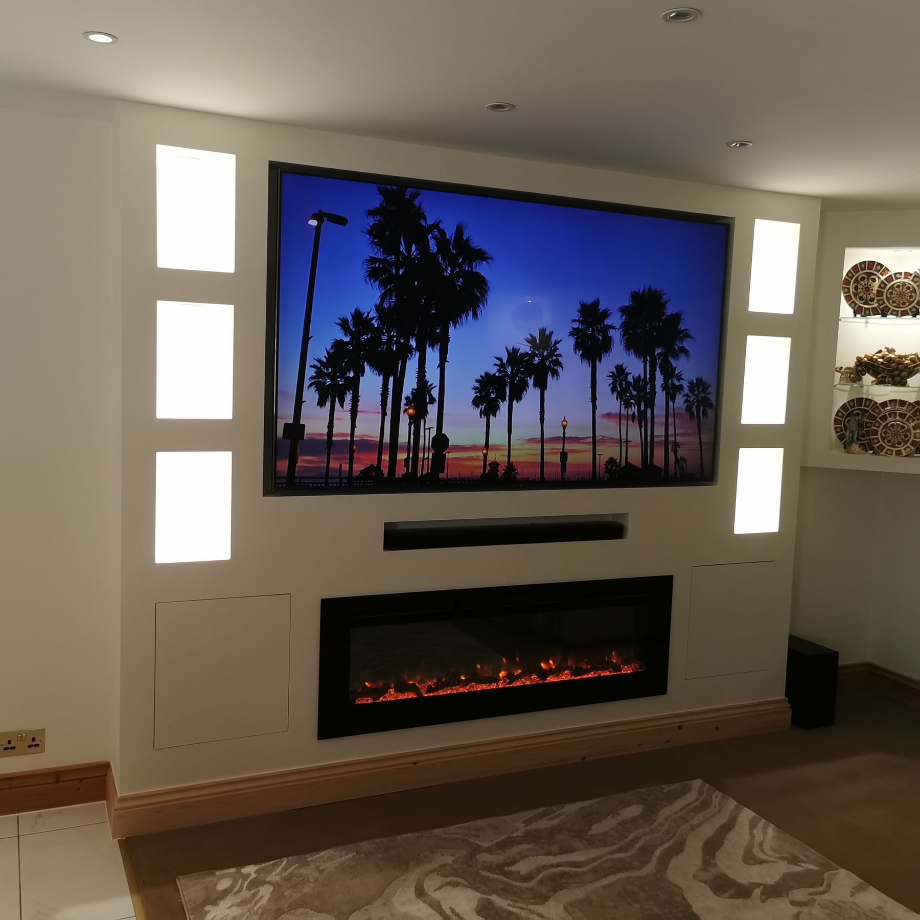 Finished media wall with vertical lit alcoves and glass display shelving
