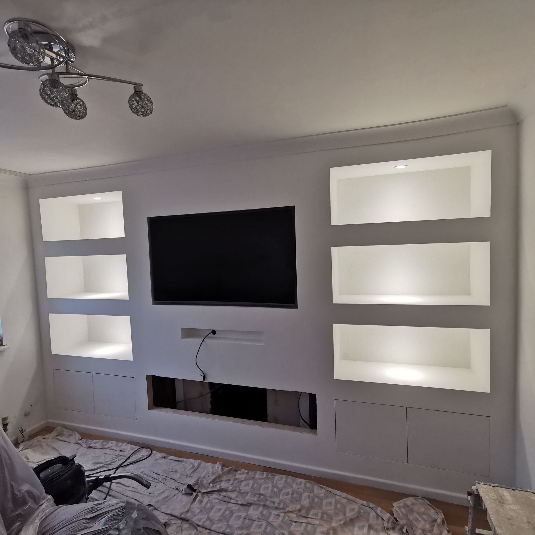 The same media wall finished, painted, with recessed TV, lit alcoves and fireplace